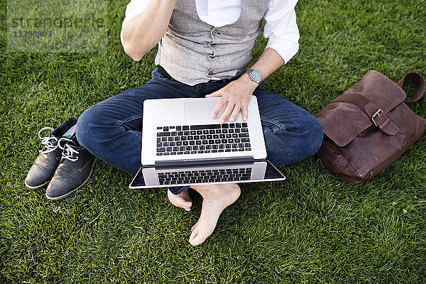 Unkenntlicher Geschäftsmann mit Laptop auf Rasen sitzend