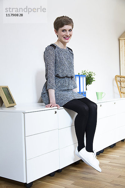 Lächelnde Frau auf Schrank im Büro sitzend