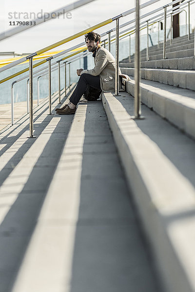Nachdenklicher Mann sitzt auf einer Treppe im Freien.