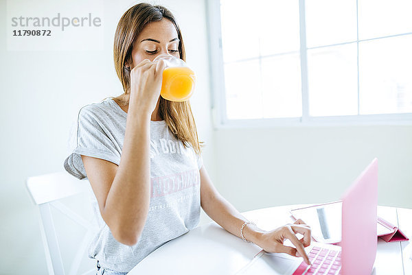 Junge Frau trinkt Orangensaft bei der Benutzung des Laptops