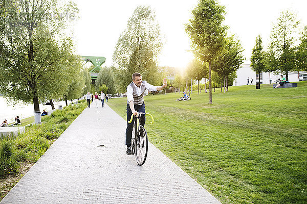Selbstbewusster  reifer Geschäftsmann auf dem Fahrrad an der Uferpromenade