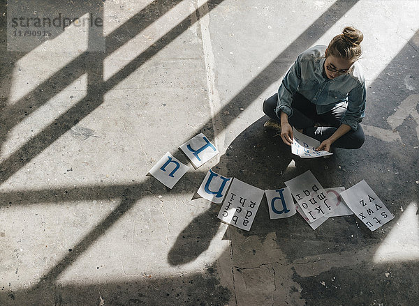 Junge Frau auf Betonboden sitzend  auf Briefvorlagen arbeitend