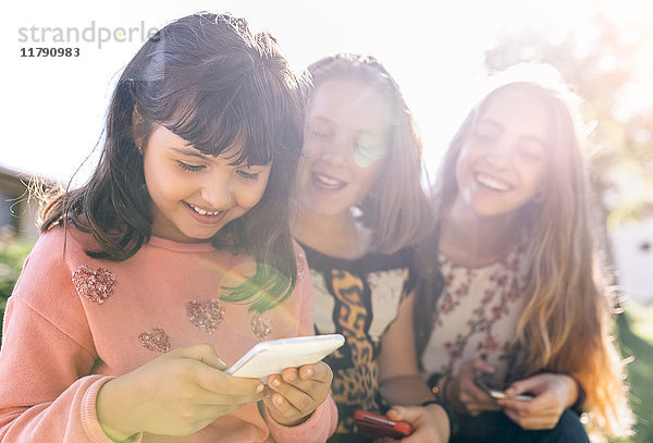 Drei glückliche Mädchen mit ihren Smartphones im Freien