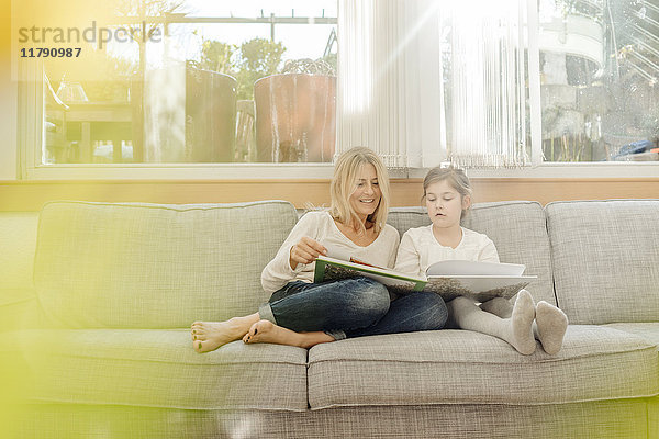 Reife Frau und Mädchen zu Hause beim Betrachten des Fotoalbums auf der Couch