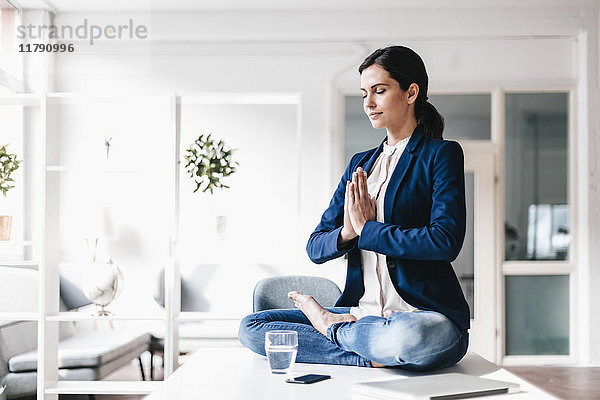 Geschäftsfrau auf dem Tisch sitzend meditierend