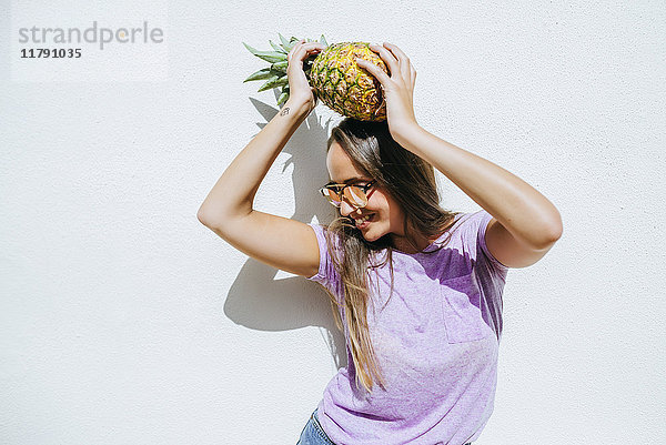 Fröhliche junge Frau hält Ananas vor weißer Wand