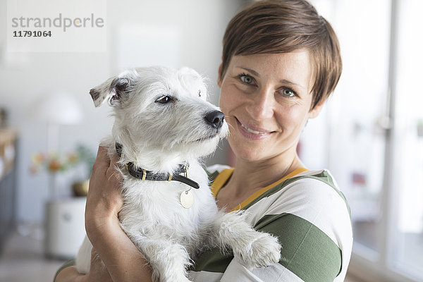 Porträt einer lächelnden Frau  die ihren Hund auf dem Arm hält.
