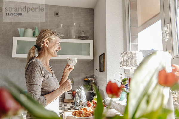 Glückliche Frau zu Hause in der Küche mit Blick aus dem Fenster