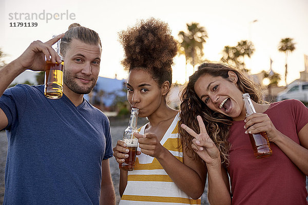 Porträt von drei Freunden mit Bierflaschen  die sich am Strand amüsieren