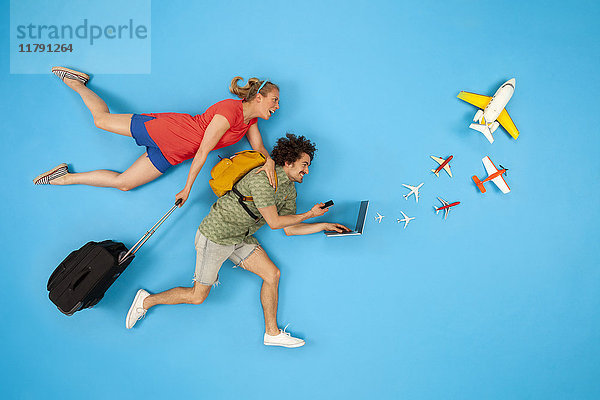 Paar mit Koffer mit Blick auf Laptop mit herauskommenden Flugzeugen