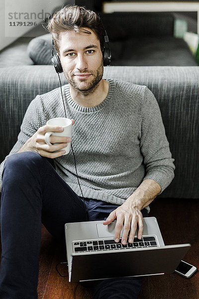 Porträt eines selbstbewussten jungen Mannes mit Laptop und Kopfhörer zu Hause