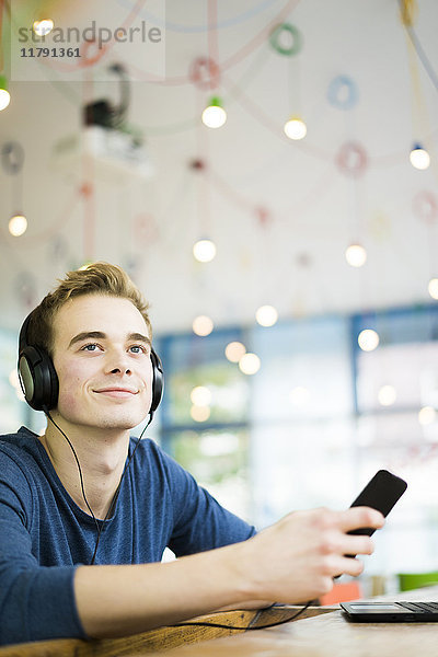 Porträt eines entspannten jungen Mannes beim Musikhören mit Kopfhörer und Smartphone im Café