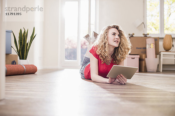 Junge Frau in neuem Zuhause auf dem Boden liegend mit Tablette