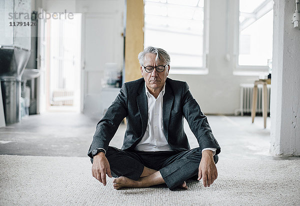 Senior Geschäftsmann auf dem Boden sitzend meditierend