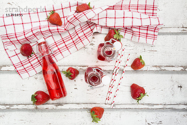 Drei Glasflaschen hausgemachte Erdbeerlimonade und Erdbeeren auf weißem Holz