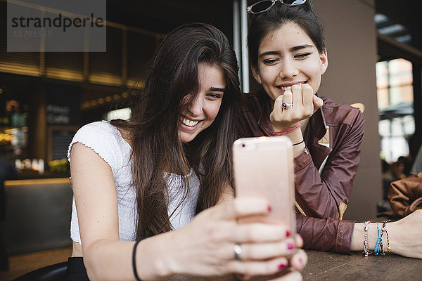 Zwei glückliche junge Frauen  die das Handy in einer Bar anschauen.