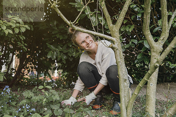 Lächelnde junge Frau beim Unkrautjäten im Garten