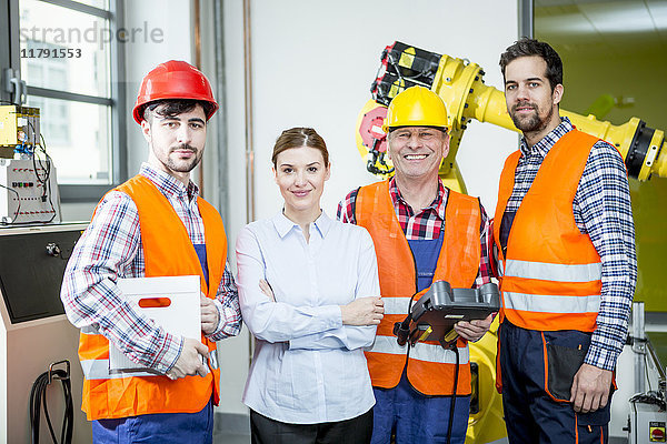 Porträt der selbstbewussten Mitarbeiter in der Fabrik mit Industrieroboter im Hintergrund