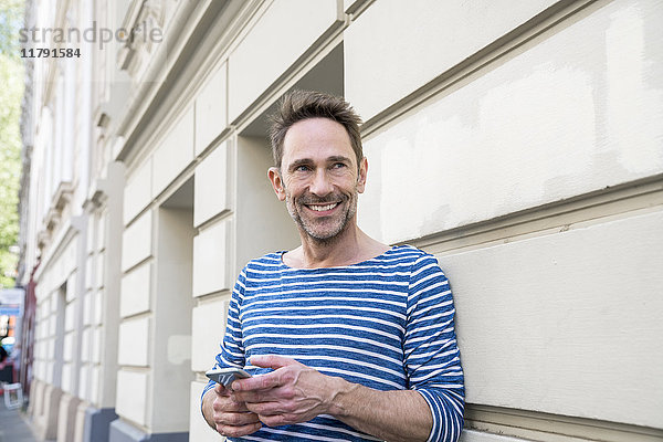Porträt des Lächelns mit an die Fassade gelehntem Smartphone