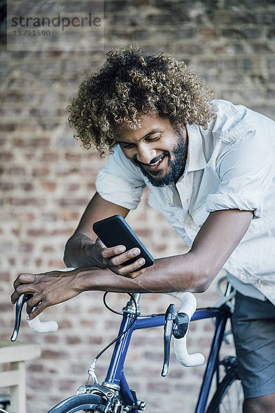 Glücklicher junger Mann mit Fahrradkontrolle Handy