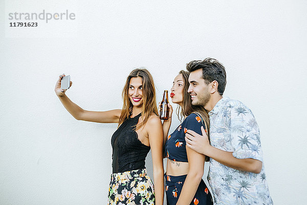 Freunde  die einen Selfie mit Smartphone vor der weißen Wand nehmen
