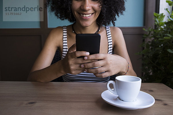 Junge Frau sitzt in einem Café und schaut auf das Smartphone.