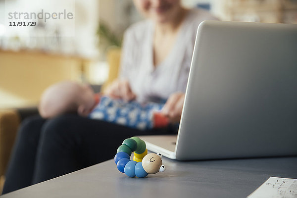 Babyspielzeug neben dem Laptop der Mutter  die ihr neugeborenes Baby zu Hause hält.