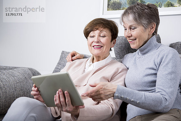 Zwei ältere Frauen sitzen auf der Couch und schauen auf das digitale Tablett.