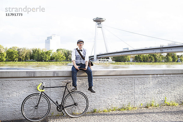 Geschäftsmann mit Fahrrad und Tablette am Flussufer
