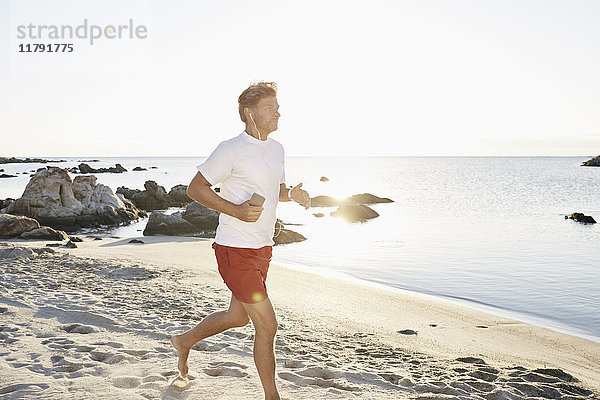 Reife Männer joggen am Strand beim Musikhören mit Smartphone und Kopfhörer