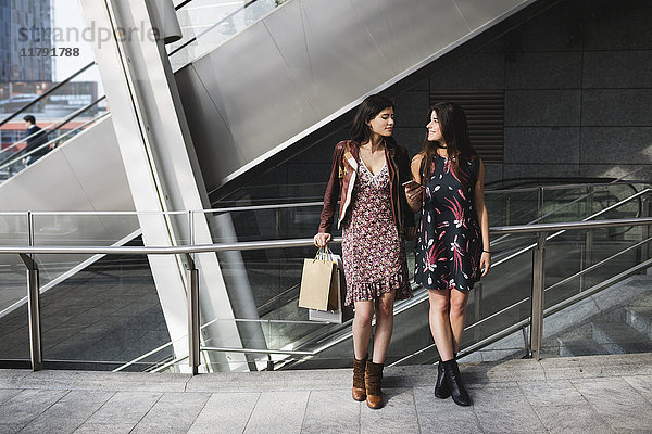 Zwei junge Frauen mit Einkaufstaschen und Handy in der Stadt