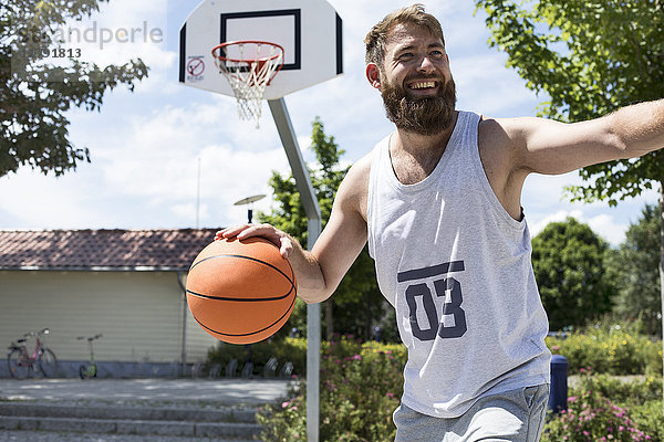 Lachender Mann beim Basketballspielen auf dem Freigelände
