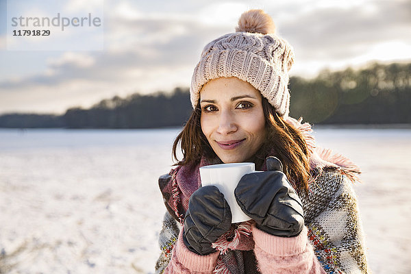 Porträt einer lächelnden Frau  die im Winter ein heißes Getränk aus einer Tasse im Freien trinkt.