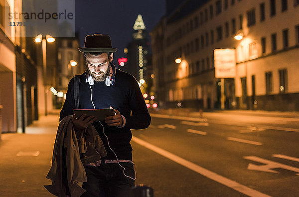 Stilvoller junger Mann mit Tablette auf der Stadtstraße bei Nacht