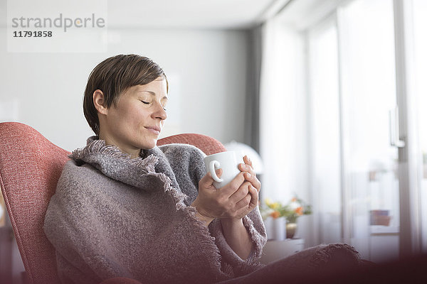 Portrait einer Frau mit geschlossenen Augen  die sich bei einer Tasse Kaffee zu Hause entspannt.