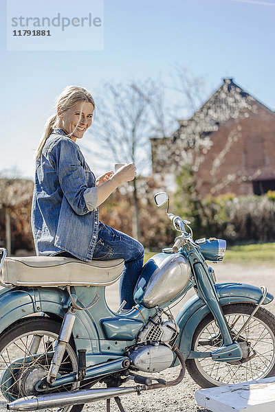 Lächelnde Frau auf Oldtimer-Motorrad bei einer Kaffeepause