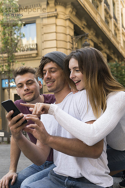 Drei Freunde  die ihr Handy in der Stadt teilen.