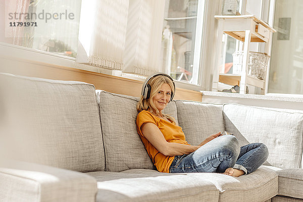 Frau zu Hause auf der Couch sitzend mit Kopfhörer