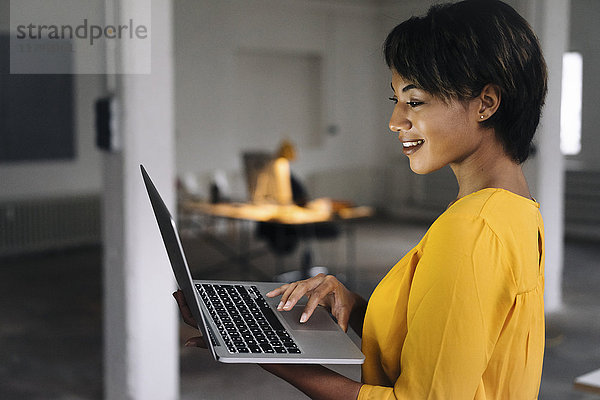 Lächelnde Frau mit Laptop im leeren Büro