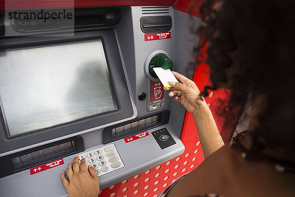 Frau schiebt Kreditkarte am Geldautomaten