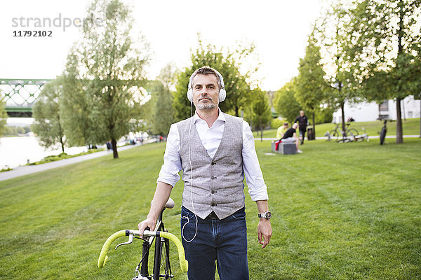Selbstbewusster Geschäftsmann mit Fahrrad und Kopfhörer im Stadtpark
