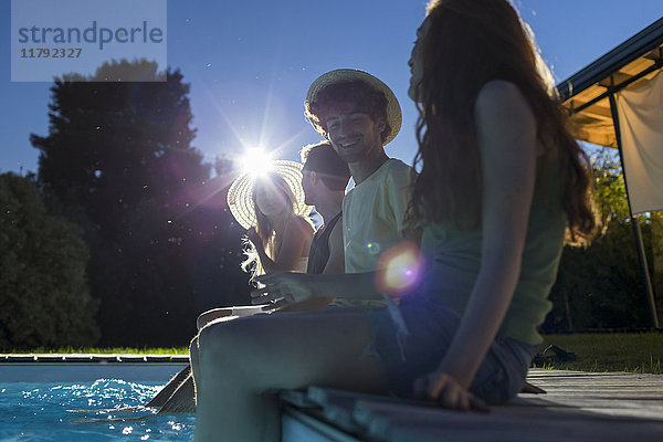 Vier Freunde sitzen in der Abenddämmerung am Pool.