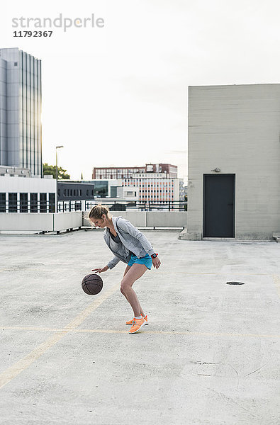 Frau spielt Basketball auf Parkdeck in der Stadt
