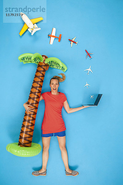 Frau hält aufblasbare Palme und Laptop mit herauskommenden Flugzeugen