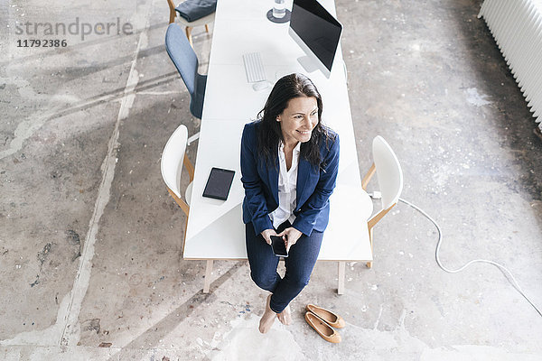 Lächelnde Geschäftsfrau sitzt auf dem Schreibtisch in einem Loft
