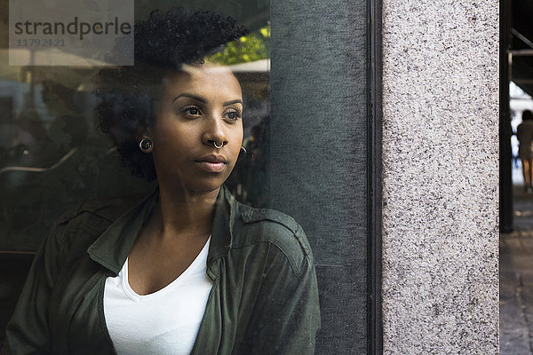 Porträt einer jungen Frau  die aus dem Fenster eines Cafés schaut.