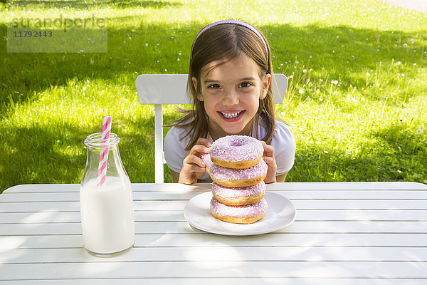 Glückliches Mädchen mit Donuts auf Gartentisch