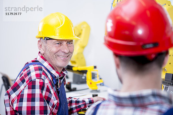 Mann in der Fabrik mit Schutzhelm lächelt Kollege an