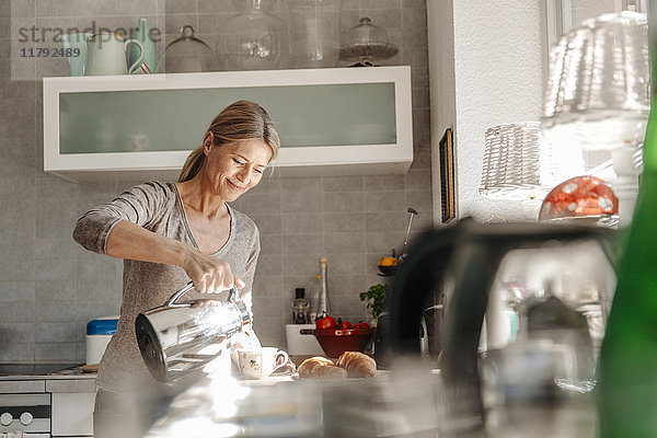 Frau zu Hause in der Küche gießt Kaffee in die Tasse