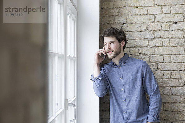 Junger Geschäftsmann am Fenster stehend  mit Smartphone